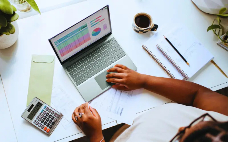 How U.S. Companies Foster Innovation and Creativity to Drive Business Success 2 Business professional analyzing charts and financial data on a laptop with reports, calculator, and coffee on desk — representing productivity, innovation, and data-driven decision-making