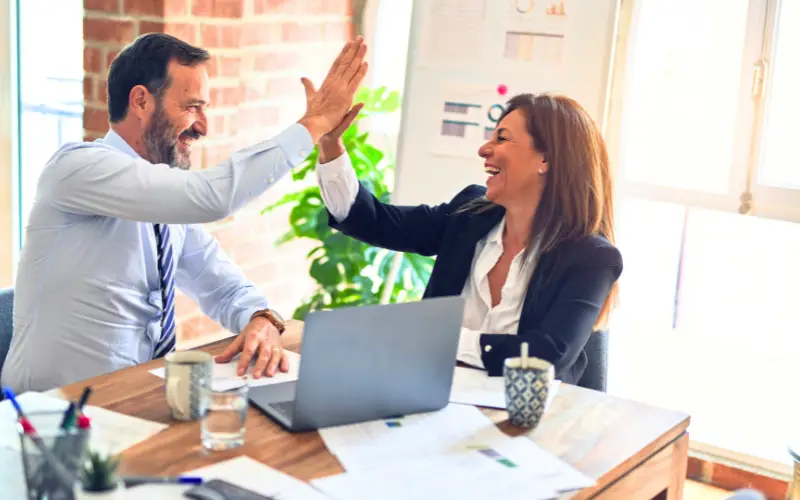 How U.S. Companies Foster Innovation and Creativity to Drive Business Success 1 “Two business professionals smiling and giving a high five in a modern office, celebrating teamwork, creativity, and business success.”
